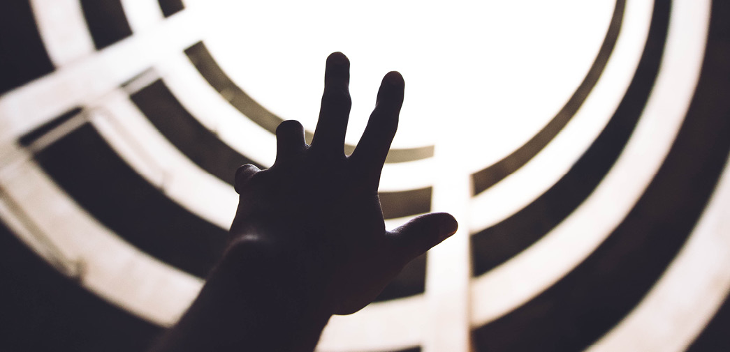 The silhouette of a hand reaches up toward light
