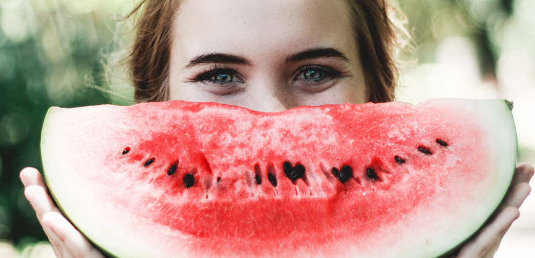 A young woman holds up a half of a watermelon