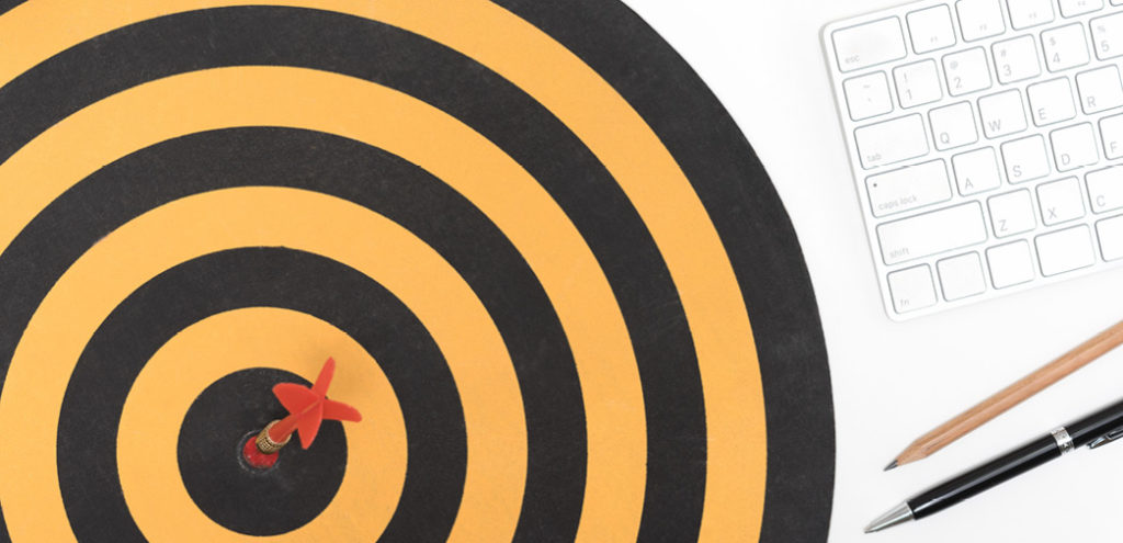 A target with a dart in the bullseye, placed on a desk beside a wireless keyboard