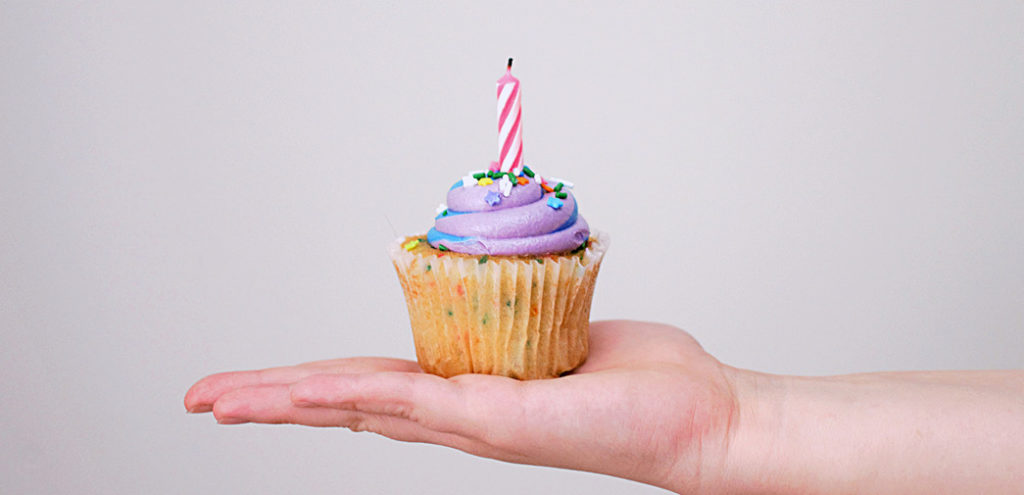 A hand holds a birthday cupcake with a candle placed on top