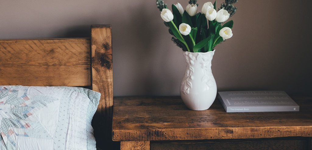 A DIY headboard and matching bedside table, which holds a vase full of flowers