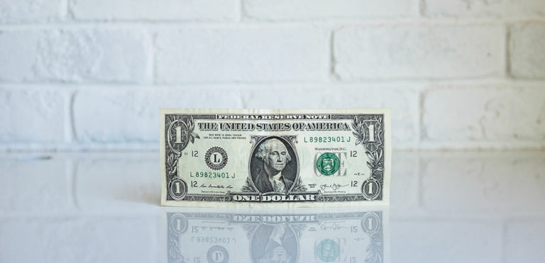 A dollar bill is posed in front of a brick wall